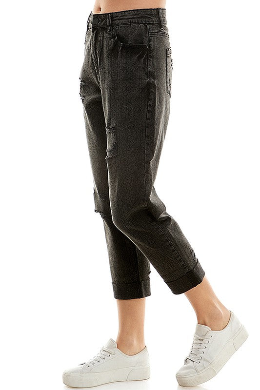 A female model wearing a white tank top and blue distressed cuffed mom jeans with a zipper closure at RIODECA.