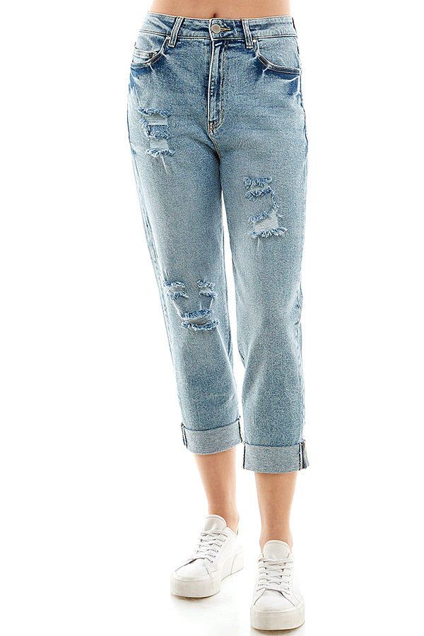 A female model wearing a white tank top and blue distressed cuffed mom jeans with a zipper closure at RIODECA.