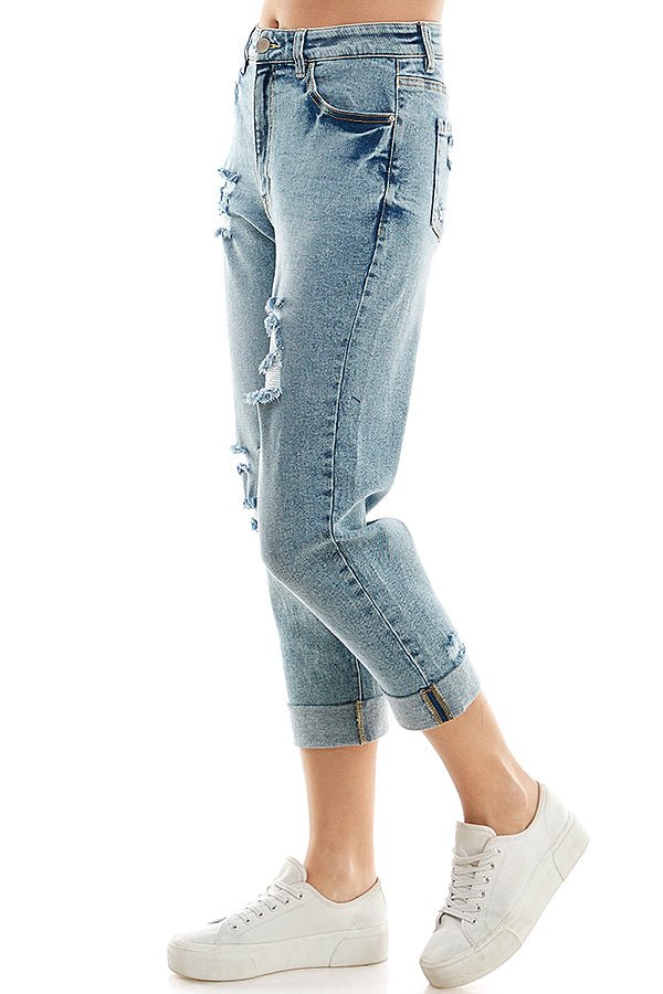 A female model wearing a white tank top and blue distressed cuffed mom jeans with a zipper closure at RIODECA.