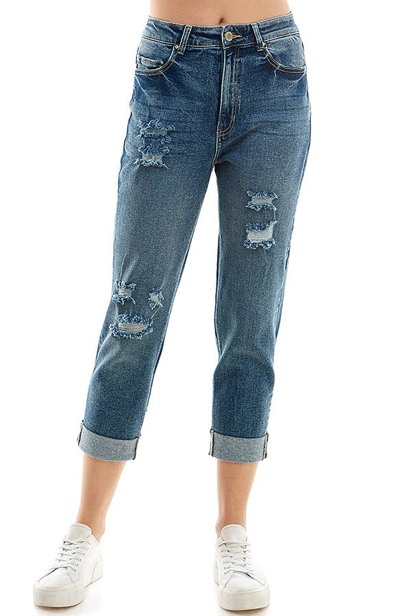 A female model wearing a white tank top and blue distressed cuffed mom jeans with a zipper closure at RIODECA.