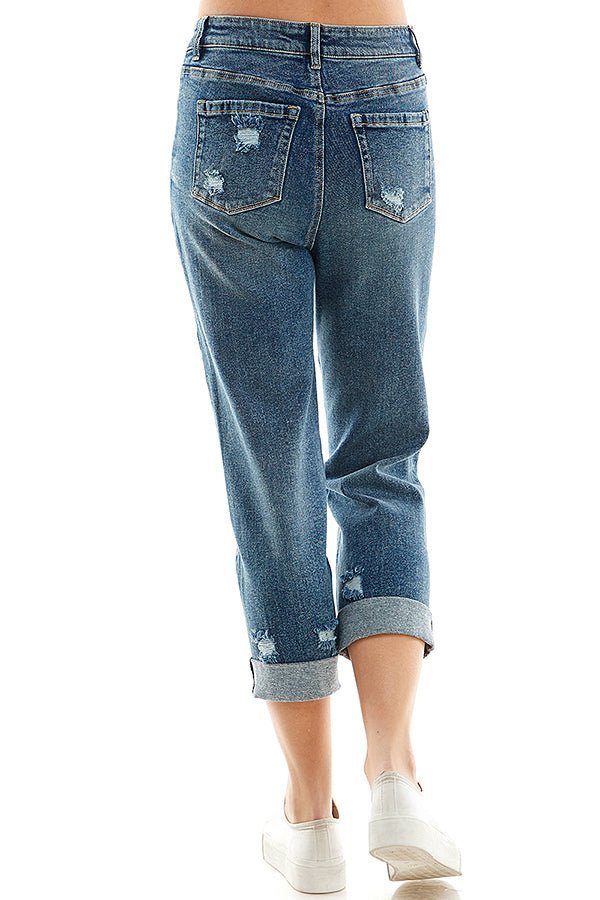 A female model wearing a white tank top and blue distressed cuffed mom jeans with a zipper closure and white converse sneakers.