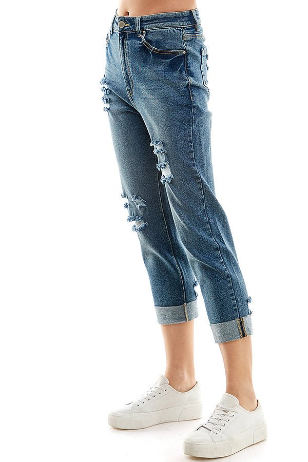 A female model wearing a white tank top and indigo blue distressed cuffed mom jeans with a zipper closure at RIODECA.